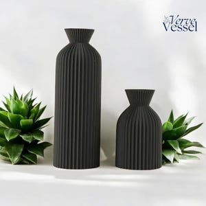 May include: Two black ceramic vases with a ribbed design. The larger vase is taller and thinner than the smaller vase.