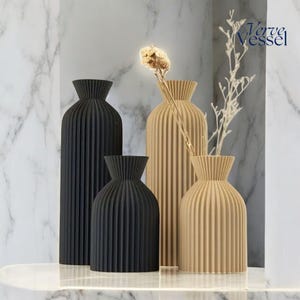 May include: Four decorative vases with a pleated design. Two vases are black and two are beige. The vases are arranged on a white surface. The text "Verve Vessel" is visible in the top right corner of the image.