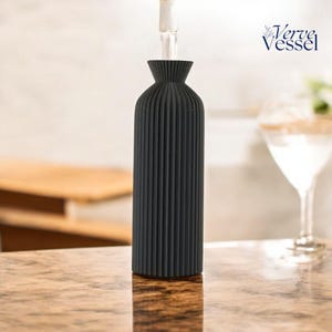 May include: A black, ribbed ceramic vase with a wide mouth and a narrow base. The vase is being filled with water from a clear glass tube.