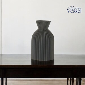 May include: A grey ceramic vase with a pleated design. The vase is sitting on a dark wooden table.