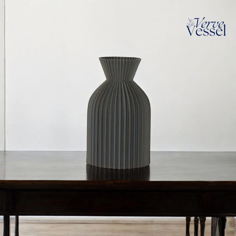 May include: A grey ceramic vase with a pleated design. The vase is sitting on a dark wooden table.