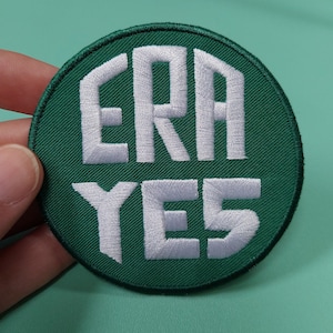 May include: A green circular patch with white embroidered text that reads "ERA YES".