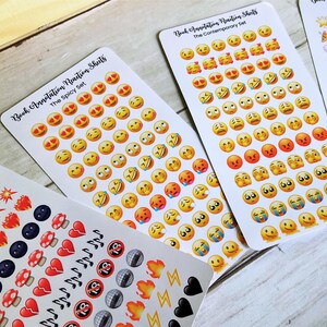 May include: Sheets of stickers with various emoji faces and other small graphics. The stickers are organized on rectangular sheets with text that reads "Book Annotation Reaction Sheets". The emoji stickers include smiling, crying, and angry faces.