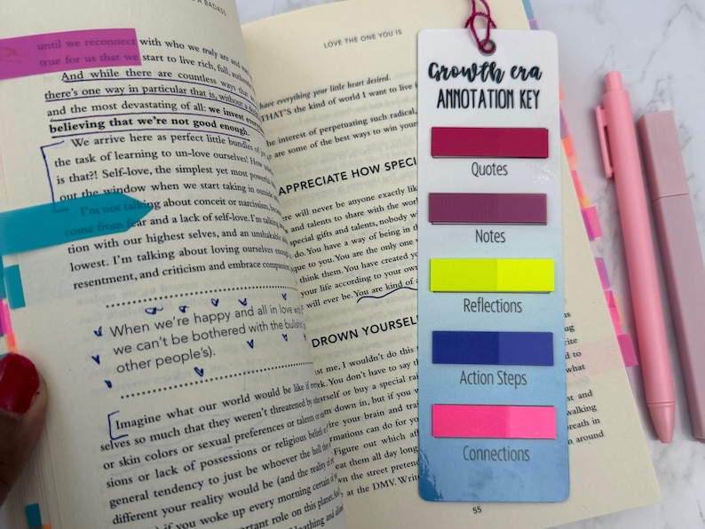 May include: A white rectangular annotation key bookmark with a pink string loop, featuring the text Growth era ANNOTATION KEY and five colored adhesive tabs labeled Quotes, Notes, Reflections, Action Steps, and Connections, placed on an open book.