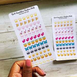 May include: Two sticker sheets with various emoji designs, including stars, hearts, bows, butterflies, and suns. The text "Book Annotation Reaction Sheets" and "The Soft Girl Set" are printed on the stickers. The stickers are held by a person.