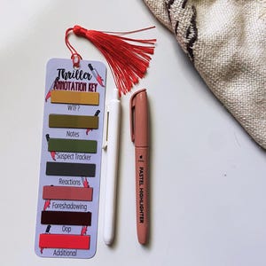 May include: A bookmark with a red tassel, labeled "Thriller Annotation Key," with color-coded sections for notes. A white pen and a pastel highlighter are next to the bookmark. The bookmark is designed for annotating thriller books.
