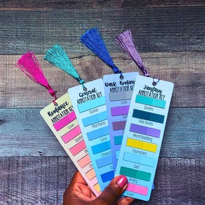 May include: Four rectangular bookmarks with annotation keys for Romance, General, Dark Romance, and Fantasy. Each bookmark features a colored tassel and printed labels for categories like Love, Quotes, and Plot Points with corresponding color-coded blocks.