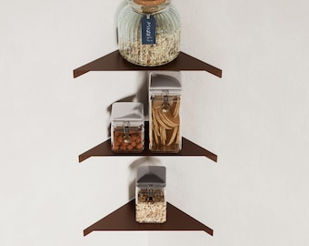 May include: A set of three brown corner shelves with various glass jars filled with food items. The shelves are mounted on a white wall, creating a modern and functional storage solution for a kitchen or pantry.