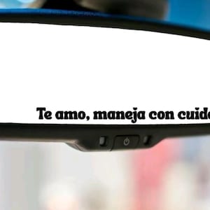 Może przedstawiać: Czarny lusterko wsteczne z hiszpańskim tekstem "Te amo, maneja con cuidado" i symbolem serca. Lusterko ma prostokątny kształt z zaokrąglonymi rogami i jest zamontowane w czarnej plastikowej obudowie. Tekst jest czarny.