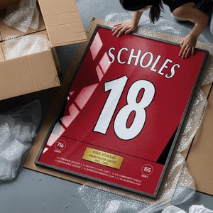 May include: A framed red sports jersey print featuring the name SCHOLES and the number 18 in white. Below, a gold plaque displays PAUL SCHOLES, MANCHESTER UNITED, 1992-2013, with statistics for 716 games and 155 goals, plus a list of major trophy titles.