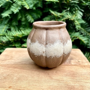 May include: A round, brown ceramic pot with a wide, open top and vertical ribbed detailing. A horizontal band of textured, off-white speckled glaze wraps around the center of the vessel, contrasting with the smooth, matte brown clay finish.