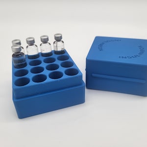 Könnte beinhalten: Ein blauer Organizer mit einem Raster von Löchern hält mehrere kleine Glasfläschchen mit silbernen Verschlüssen. Eine passende blaue Box mit dem Text "INSULINBOX" befindet sich neben dem Organizer. Die Fläschchen sind mit einer klaren Flüssigkeit gefüllt.