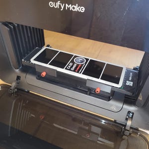 Könnte beinhalten: Ein schwarzer und grauer 3D-Drucker mit dem Text "eufy Make" oben. Im Inneren befindet sich eine rechteckige Plattform mit einem schwarz-weißen Design und dem Text "CA-3D GmbH". Rote und schwarze Komponenten sind sichtbar.