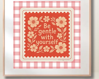 May include: A framed print featuring a red postage stamp design with the words "Be gentle with yourself" surrounded by floral illustrations. The background is a pink and white gingham pattern.