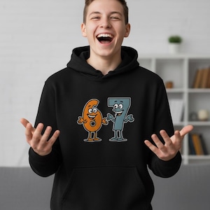 May include: Black hooded sweatshirt featuring a cartoon graphic of the numbers six and seven with smiling faces. The numbers are orange and blue, outlined in black. The sweatshirt has a front pocket.