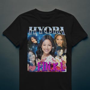 May include: Black t-shirt featuring a graphic of a woman with multiple images of her face, the text "HYORI" in a blue and white font, and the text "FIN.K.L" in pink. The design includes a heart and lightning bolts.