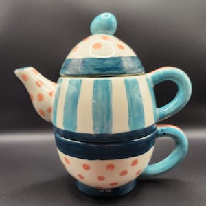 May include: A white ceramic teapot and cup set with blue and orange stripes and polka dots. The teapot has a lid with a blue knob.