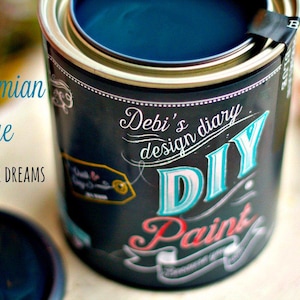 Puede incluir: Una lata de pintura DIY azul bohemio con el texto "Debi's diary design DIY Paint". La pintura es de color azul oscuro. La lata es negra con letras blancas, turquesas y rojas. Un pincel es visible en el fondo.