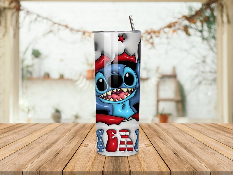 K&ouml;nnte beinhalten: Edelstahlbecher mit einem Cartoon-Charakter mit blauem K&ouml;rper, gro&szlig;en Augen und einem breiten Grinsen. Das Design enth&auml;lt rote und wei&szlig;e Akzente, mit dem Wort "USA" in einer patriotischen Schriftart. Ein silberner Strohhalm ist eingesetzt.