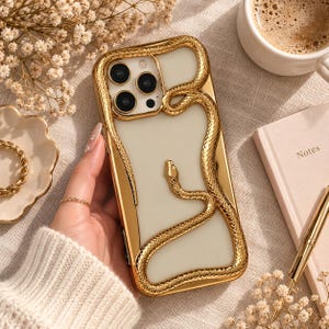 Pode incluir: Uma capa transparente para smartphone com um design de serpente dourada metálica que envolve o módulo da câmara e se estende pelo painel traseiro. A serpente tem uma superfície texturizada com escamas e aspeto tridimensional.