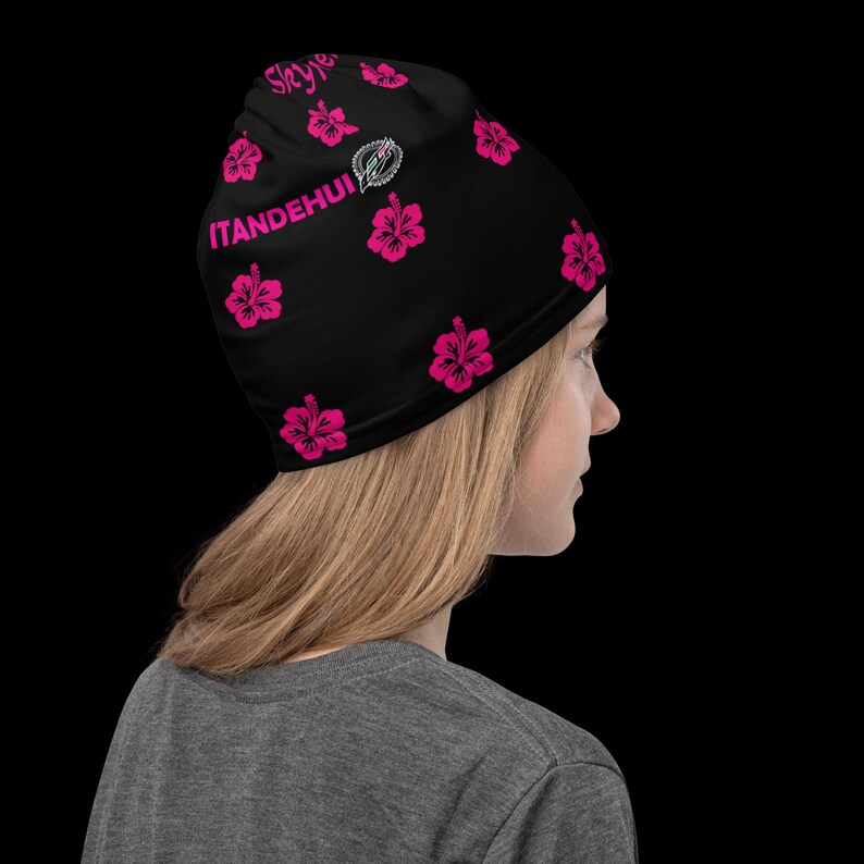 May include: A black beanie featuring a repeating pattern of bright pink hibiscus flowers. The text ITANDEHUI is printed in pink on the side, accompanied by a small circular logo graphic. The fabric is smooth and fitted, covering the head completely.