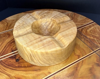 May include: A round wooden ashtray with a deep well in the center. The ashtray is made of light brown wood with a natural grain pattern.