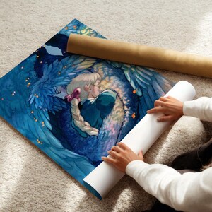 May include: A vibrant art print featuring a couple embracing, surrounded by blue feathered wings. The artwork is on a square canvas, with a rolled-up poster tube beside it. The print is on a light-colored carpet.