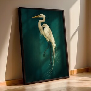 May include: A framed art print featuring a white egret against a teal background. The bird is depicted with long, flowing tail feathers and a curved neck. The artwork is in a black frame and leans against a wall.