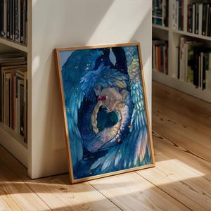 May include: A framed art print featuring a watercolor illustration of two figures embracing, surrounded by blue and teal feathered wings. The artwork has a celestial theme with gold accents and is displayed on a wooden floor.