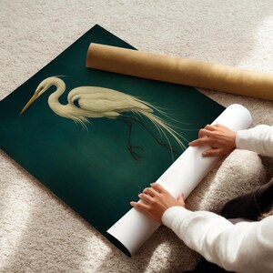 May include: An art print of a white egret with a long, curved neck and flowing tail feathers, set against a dark teal background. A rolled-up white print and a brown tube are also visible.