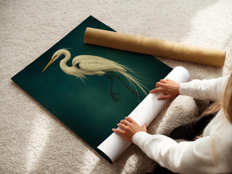 May include: An art print of a white egret with a long, curved neck and flowing tail feathers, set against a dark teal background. A rolled-up white print and a brown tube are also visible.