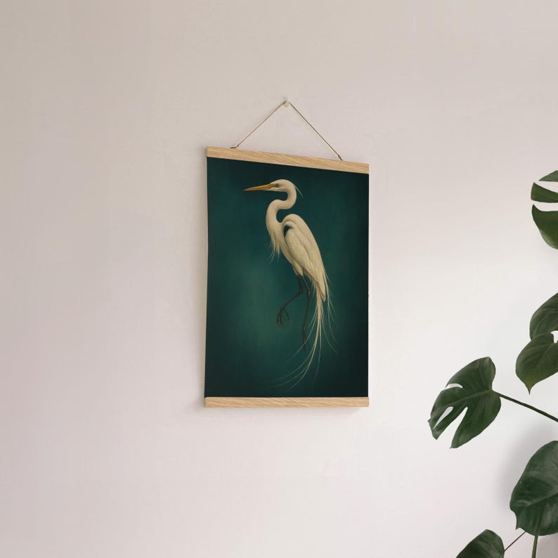 May include: A framed wall art print featuring a white egret bird against a dark teal background. The bird is depicted in a realistic style with long, flowing feathers. The frame is made of light-colored wood, and the artwork is suspended by a string.