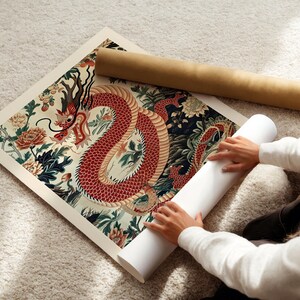 May include: A person is rolling up a print of a red dragon with intricate details on a white background. The dragon is surrounded by green and blue floral patterns.