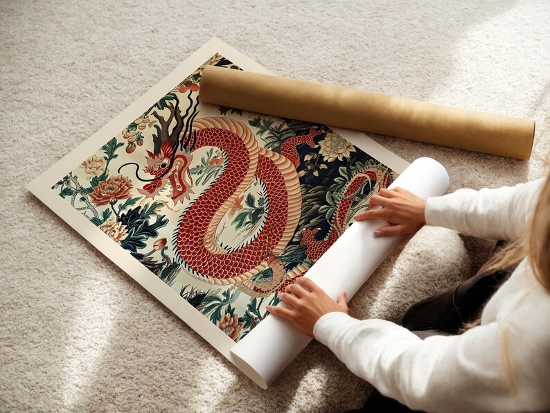 May include: A person is rolling up a print of a red dragon with intricate details on a white background. The dragon is surrounded by green and blue floral patterns.