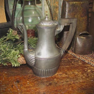 May include: A silver teapot with a wooden handle. The teapot has a fluted design and a rounded body. It is sitting on a wooden table.