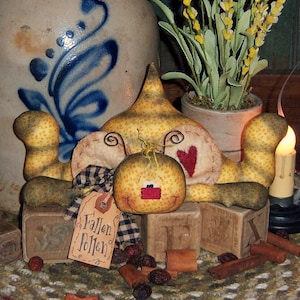 May include: A handmade yellow felt bee with a red heart and a black eye. The bee is lying on top of wooden blocks with the text "Fallen Pollen" on a tag.