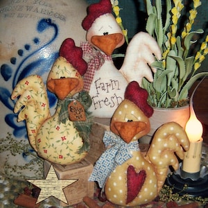 May include: Three handmade fabric chickens with a yellow, white, and red color scheme. The chickens are sitting on a wooden box with a sign that says "Farm Fresh".