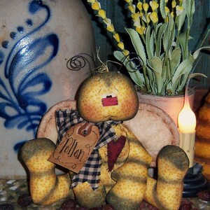 May include: A handmade rag doll bee with a yellow and brown striped body, a red heart on its chest, and a tag that says "Pollen". The bee is sitting on a brown and white rug with dried berries scattered around it.