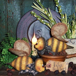 May include: Two handmade felt bee figurines with black and white plaid ribbon accents. The bees are sitting in a wooden bowl with a brown tag that reads "Pollen Peddlers!" The bowl is surrounded by small brown berries.