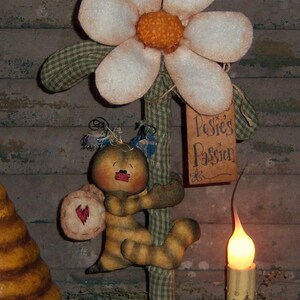 May include: A handmade fabric bee doll climbing a green and white gingham fabric stalk with a white fabric flower on top. The flower has a yellow center and a sign that reads "Posy's Passion".