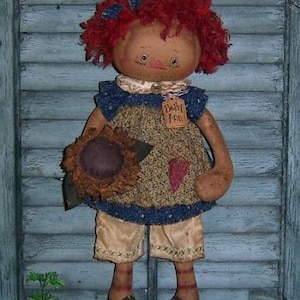 May include: A handmade rag doll with red curly hair, a blue and brown dress, and a sunflower in her hand. The doll is wearing a tag that says "Dolly Ann".