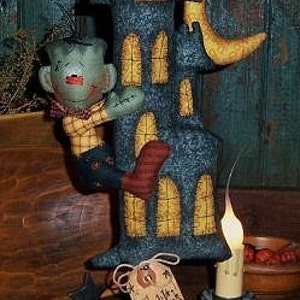May include: A Halloween-themed decorative piece featuring a dark blue castle with yellow window accents and a crescent moon. A green Frankenstein figure is attached to the castle. A tag reads "Frankie's Manor". Small orange pumpkins are scattered around the base.