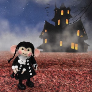May include: A small, black and white felt mouse doll wearing a black coat with white buttons and a white collar. The doll has pink cheeks and black eyes. The doll is standing in front of a dark, foggy, silhouette of a house with lit windows.