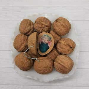 May include: A white plate with a collection of walnuts, one of which has been cracked open to reveal a small, felt mouse inside.
