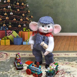 May include: A felt mouse figurine wearing a blue and white striped engineer cap and matching overalls with a red patterned neckerchief. The mouse holds a small wooden object and stands near a miniature toy train with three colorful cars.
