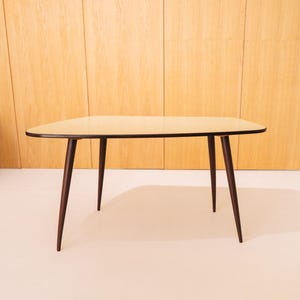 Könnte beinhalten: Ein moderner Couchtisch aus der Mitte des Jahrhunderts mit einer hellbraunen ovalen Tischplatte und dunkelbraunen, sich verjüngenden Beinen.