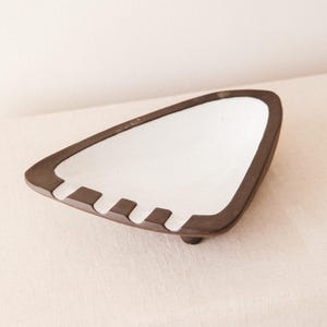 May include: A triangular ashtray with a white interior and a dark brown exterior. The ashtray has three slots for cigarettes and a small foot. The design is minimalist and modern.