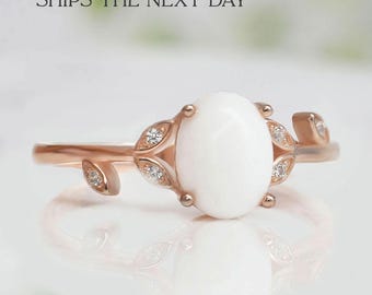 Puede incluir: Un anillo de oro rosa con una piedra de ópalo blanco y pequeños diamantes engastados en acentos en forma de hoja.