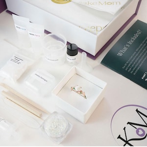 breastmilk jewelry DIY kit box with instructions, measuring and mixing tools, resin and syringe and ring in a ring box outside of the purple diy kit box for breastmilk jewelry keepsakes from KeepsakeMom
