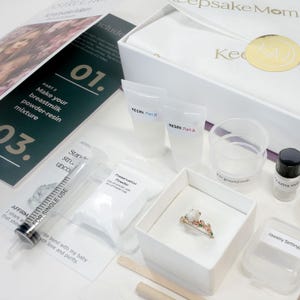 breastmilk jewelry DIY kit box with instructions, measuring and mixing tools, resin and syringe and ring in a ring box outside of the purple diy kit box for breastmilk jewelry keepsakes from KeepsakeMom